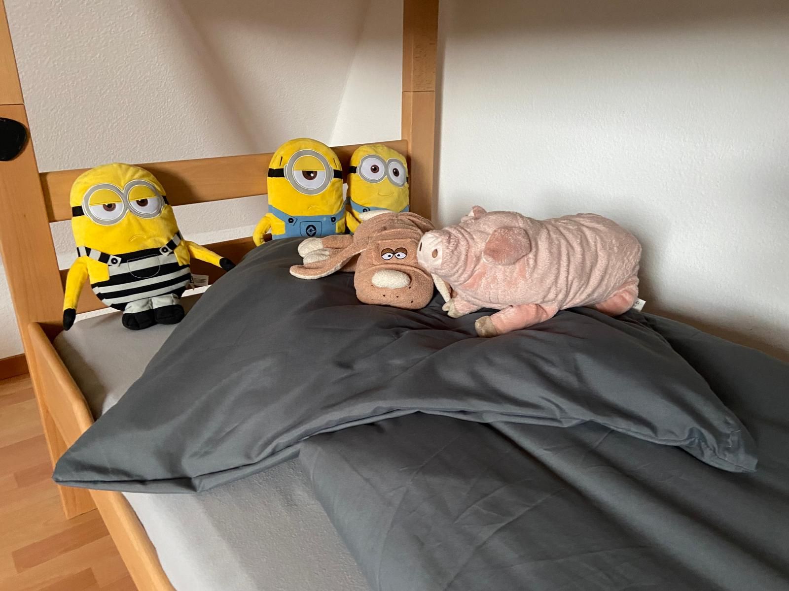 Un lit avec un matelas et des oreillers gris, une tête de lit en bois et trois peluches posées sur le lit.