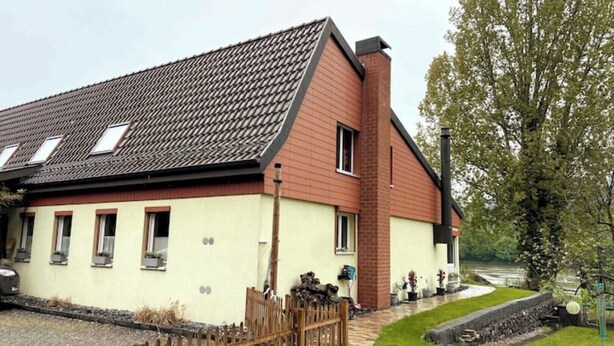 Un bâtiment à deux étages, doté d’un toit en pente, d’une cheminée en briques et de nombreuses fenêtres.