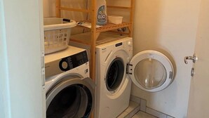 Une buanderie équipée d’une étagère en bois, de deux machines à laver, d’un sèche-linge et d’une autre machine à laver dotée d’un panneau de commande.