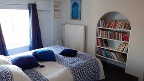 A bedroom with a bed, a bookshelf, a window with curtains, and a radiator. - Le Toit de Charme D'isabelle ! (Beaune)