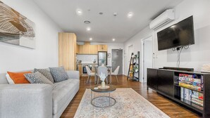 A modern living room with a grey sofa, a coffee table, and a bookshelf. - Ellerslie Sanctuary | Luxury Apt & Great Amenities (Auckland)
