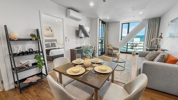 A modern hotel room with a dining area, a sofa, and a bed. - Ellerslie Sanctuary | Luxury Apt & Great Amenities (Auckland)