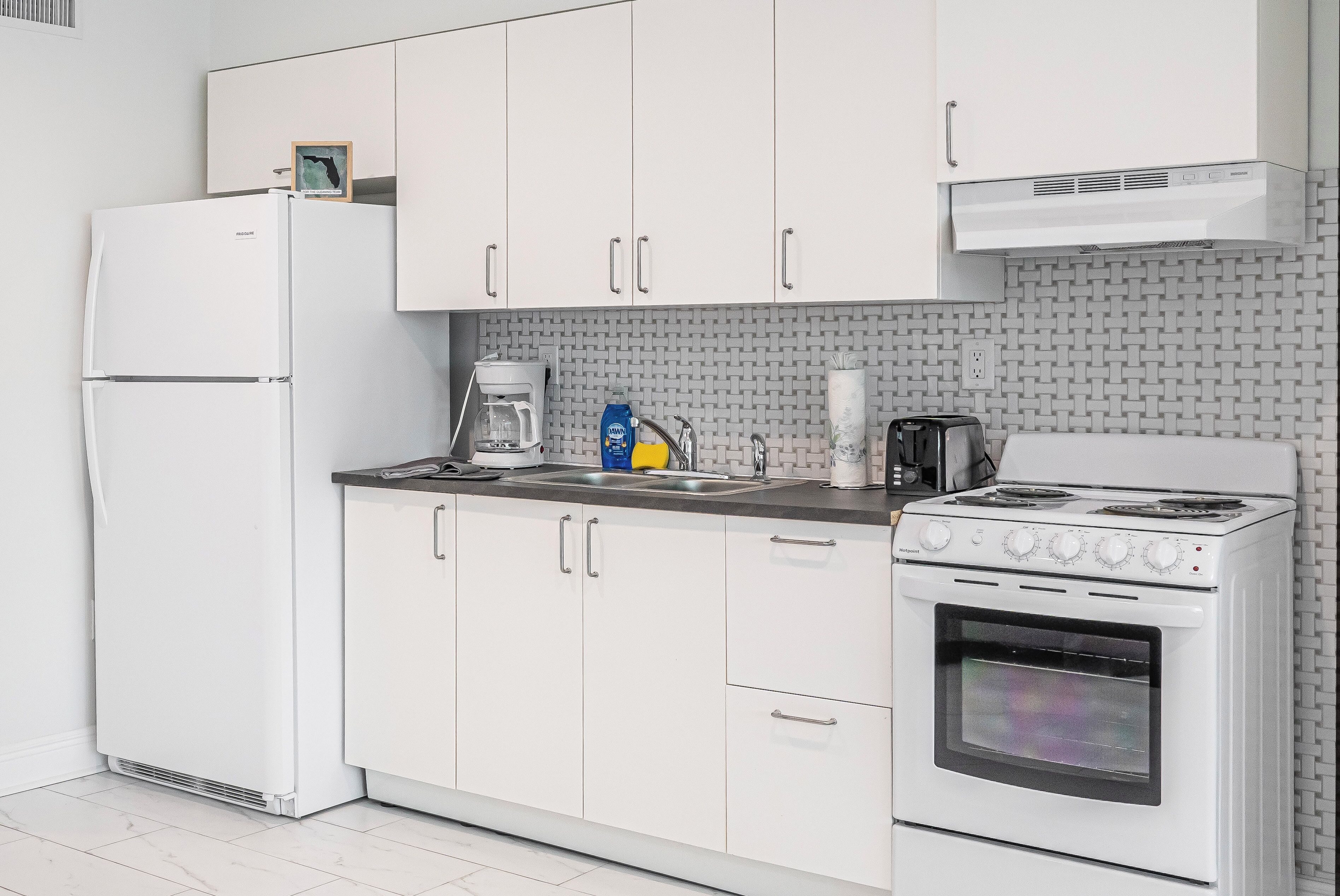 A modern kitchen with white cabinets, a refrigerator, a stove, and a coffee maker.