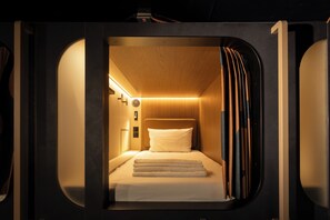 Quarto compacto e moderno com cama, cabeceira e luminária fixada na parede.