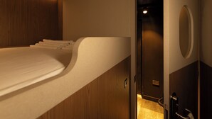 A compact, modern room with a built-in bed, a wooden panel wall, and a small, enclosed bathroom area. - Kabannas London St Pancras (London)