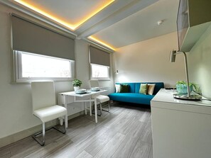 Ein modernes, helles Zimmer mit Esstisch, Stühlen, einer Couch und einem Heizkörper.