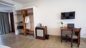 A hotel room with a wooden desk, a television, a mini-fridge, a wardrobe, and a shoe rack. - DACO Hotel (Siem Reap)