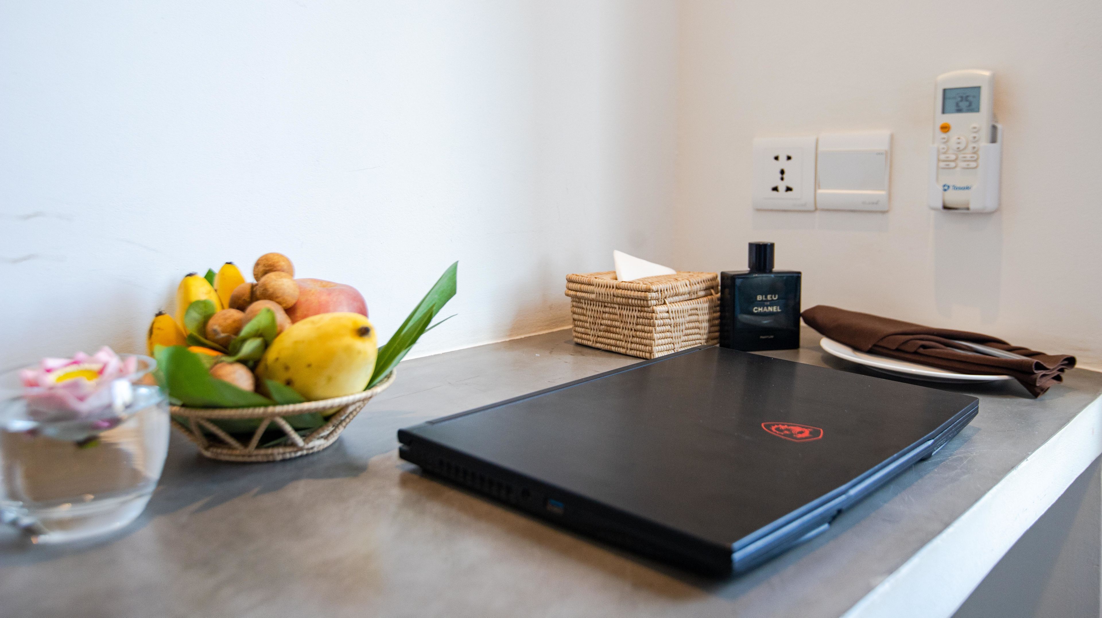 A laptop on a table with a fruit bowl, a bottle of perfume, and a napkin.