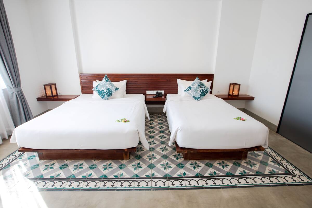 A double room with two beds, a wooden headboard, bedside tables with lamps, and a patterned floor.
