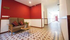 Eine Hotelhalle mit roter Wand, einer Couch mit Kissen, einem kleinen Tisch mit Pflanze und einem gemusterten Boden.