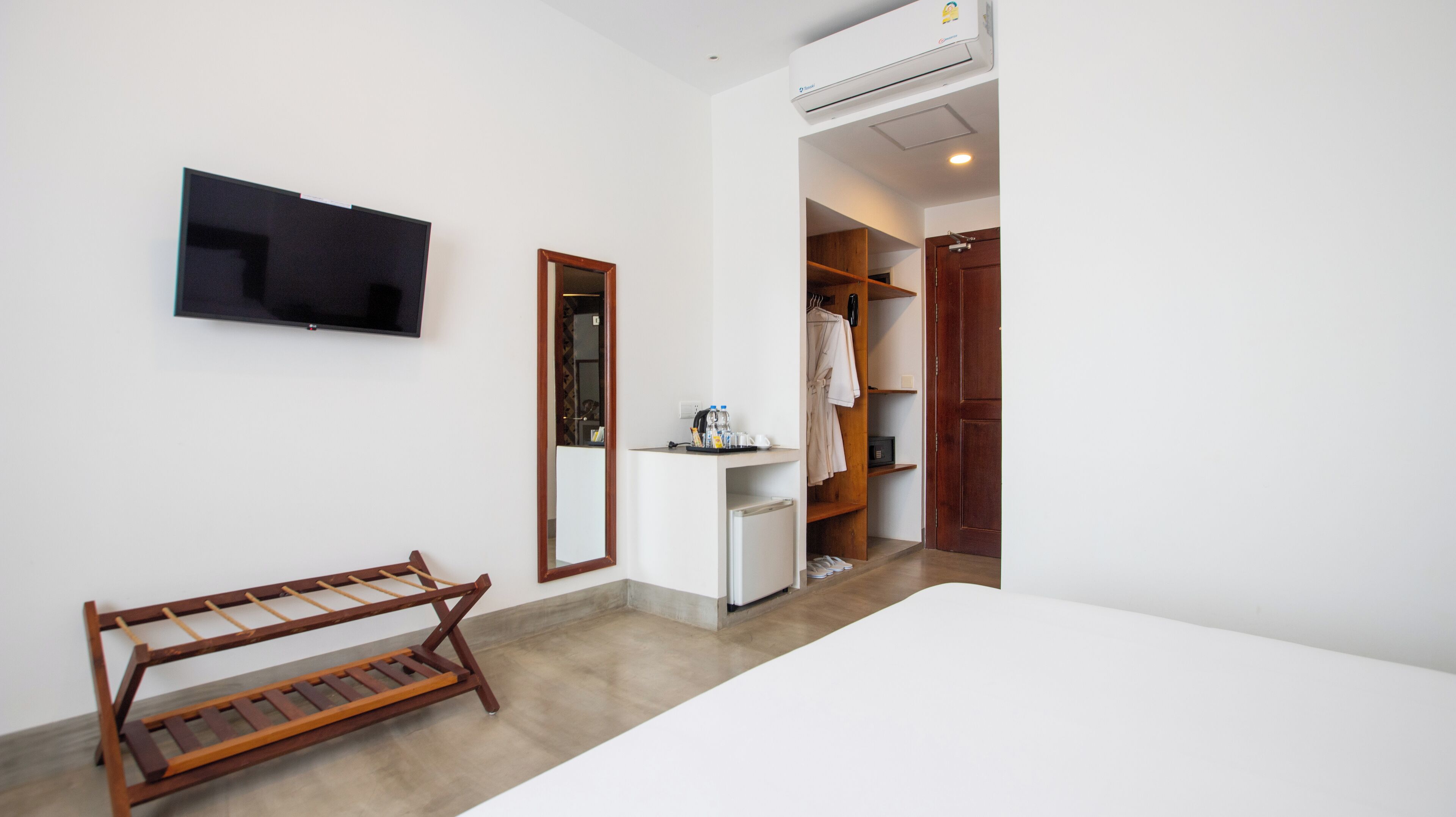 A hotel room with a bed, a TV, a wooden drying rack, a small desk with a mirror, and a wardrobe.