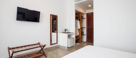 A hotel room with a bed, a TV, a wooden drying rack, a small desk with a mirror, and a wardrobe.