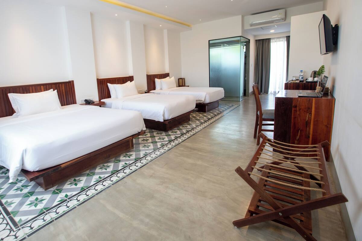 A hotel room with three beds, a desk with a laptop, a chair, and a large mirror.