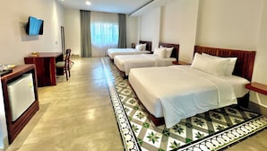 A hotel room with three beds, a desk, a television, and a patterned floor. - DACO Hotel (Siem Reap)