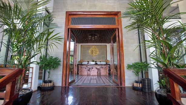 A reception area with a wooden reception desk, a large decorative tree mural, and potted plants. - DACO Hotel (Siem Reap)