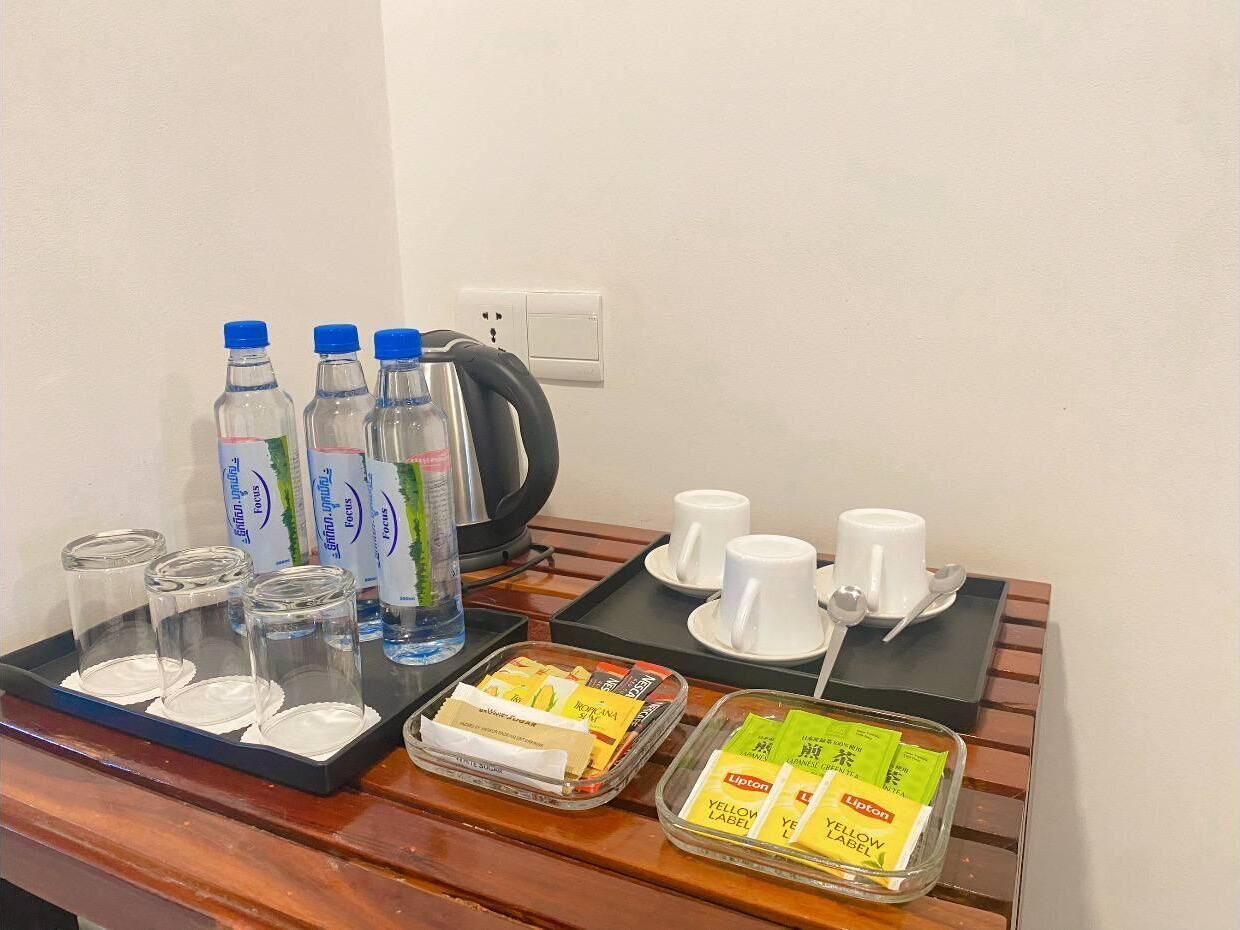 En morgenmadsanretning med vand på flaske, kaffe, te og Lipton teposer på et fad.