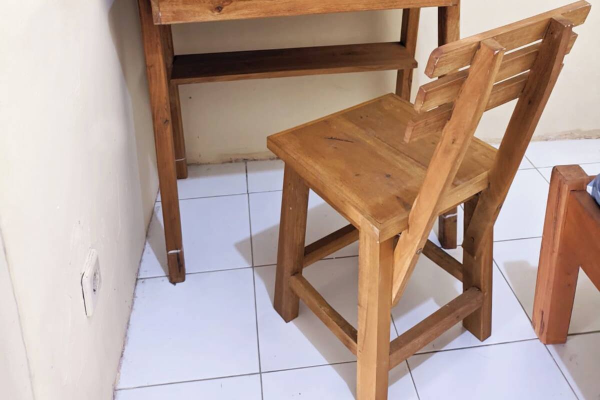 Een houten bureau en stoel voor een effen muur, met witte betegelde vloer.