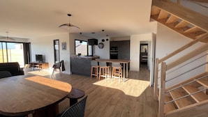 A modern kitchen with dark cabinets, a wooden dining table, and a staircase. - Maison de Vacances à 200 m de L'aber Benoît (Landéda)