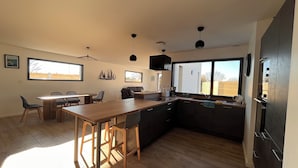 A modern kitchen with a wooden island, dark cabinetry, and pendant lighting. - Maison de Vacances à 200 m de L'aber Benoît (Landéda)