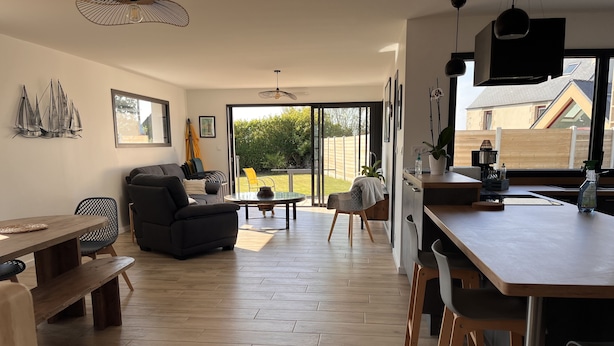 A modern kitchen with a wooden countertop, a dining area with a bench, and a living room with a sofa and chairs. - Maison de Vacances à 200 m de L'aber Benoît (Landéda)