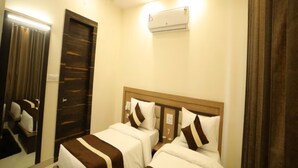 A hotel room with two beds, a ceiling fan, an air conditioning unit, and a mirror. - Hotel Amber  (Thanesar)