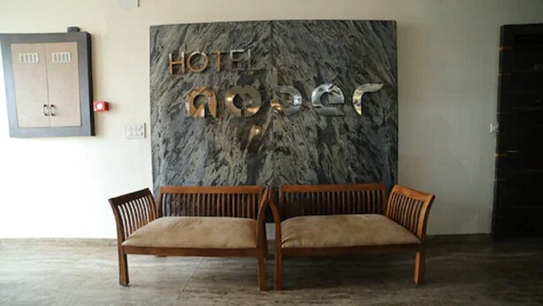 A hotel lobby with a marble wall and two wooden sofas. - Hotel Amber  (Thanesar)