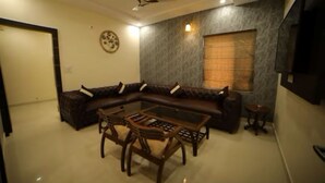 A living room with a sectional sofa, a glass coffee table, and a small side table. - Hotel Amber  (Thanesar)