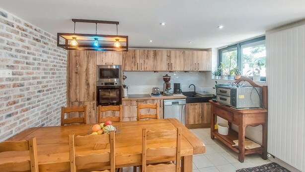 A compact kitchen with wooden cabinets, a dining table with chairs, a built-in oven, a coffee maker, and a toaster.