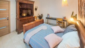 A bedroom with a bed, a desk, a chair, a TV, and a lamp.