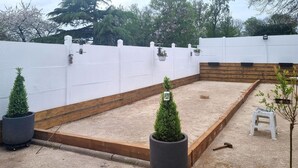 A small, enclosed garden area with a gravel surface, wooden borders, and potted plants.