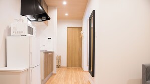 Un corridoio stretto con pavimento in legno, un frigorifero bianco, un forno a microonde e una porta in legno in fondo.