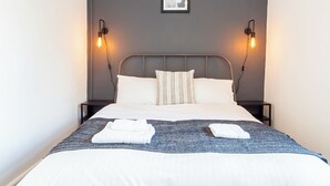 A neatly made bed with a gray headboard, two bedside lamps, and a framed picture on the wall. - City Centre 3-Bed Apartment – Sleeps up to 8 guests, with NCP car park next door (pay for parking). Walking distance to the Mayflower Theatre, shops, and transport. Ideal for families, groups, or business stays. (Southampton)