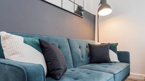 A teal sofa with multiple cushions against a dark wall, a floor lamp, and a framed artwork above. - City Centre 3-Bed Apartment – Sleeps up to 8 guests, with NCP car park next door (pay for parking). Walking distance to the Mayflower Theatre, shops, and transport. Ideal for families, groups, or business stays. (Southampton)