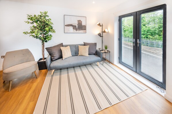 A modern living room with a grey sofa, striped rug, and a large window with a view of greenery.