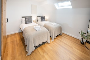 A bedroom with two beds, wooden flooring, a skylight, and a potted plant.