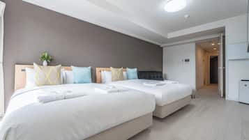 A hotel room with two beds, a grey wall, a ceiling light, and a door leading to a bathroom.