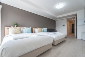 Een hotelkamer met twee bedden, een grijze muur, een plafondlamp en een deur naar een badkamer.