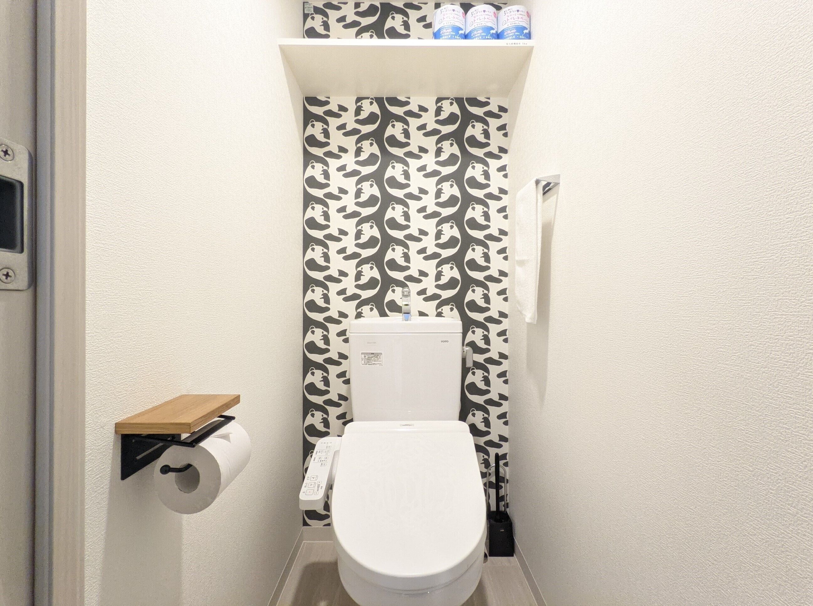 A small bathroom with a toilet, a toilet paper holder, and a shelf above the toilet.