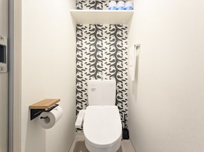 Une petite salle de bain comprenant des toilettes, un porte-rouleau de papier toilette et une étagère au-dessus des toilettes.