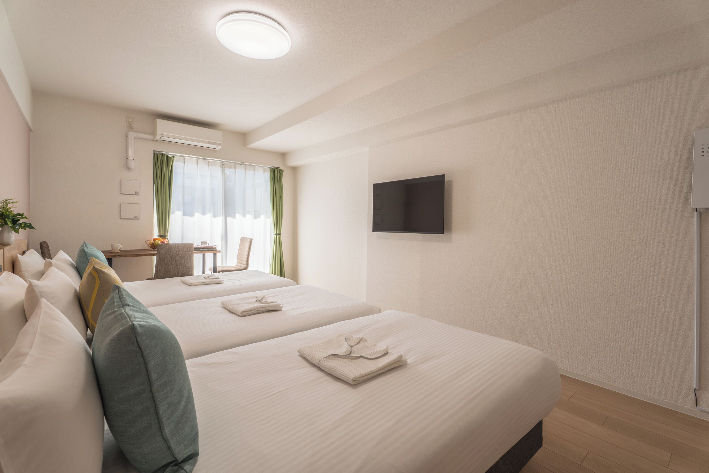 A hotel room with two beds, a desk, a chair, a TV, and a window with curtains.