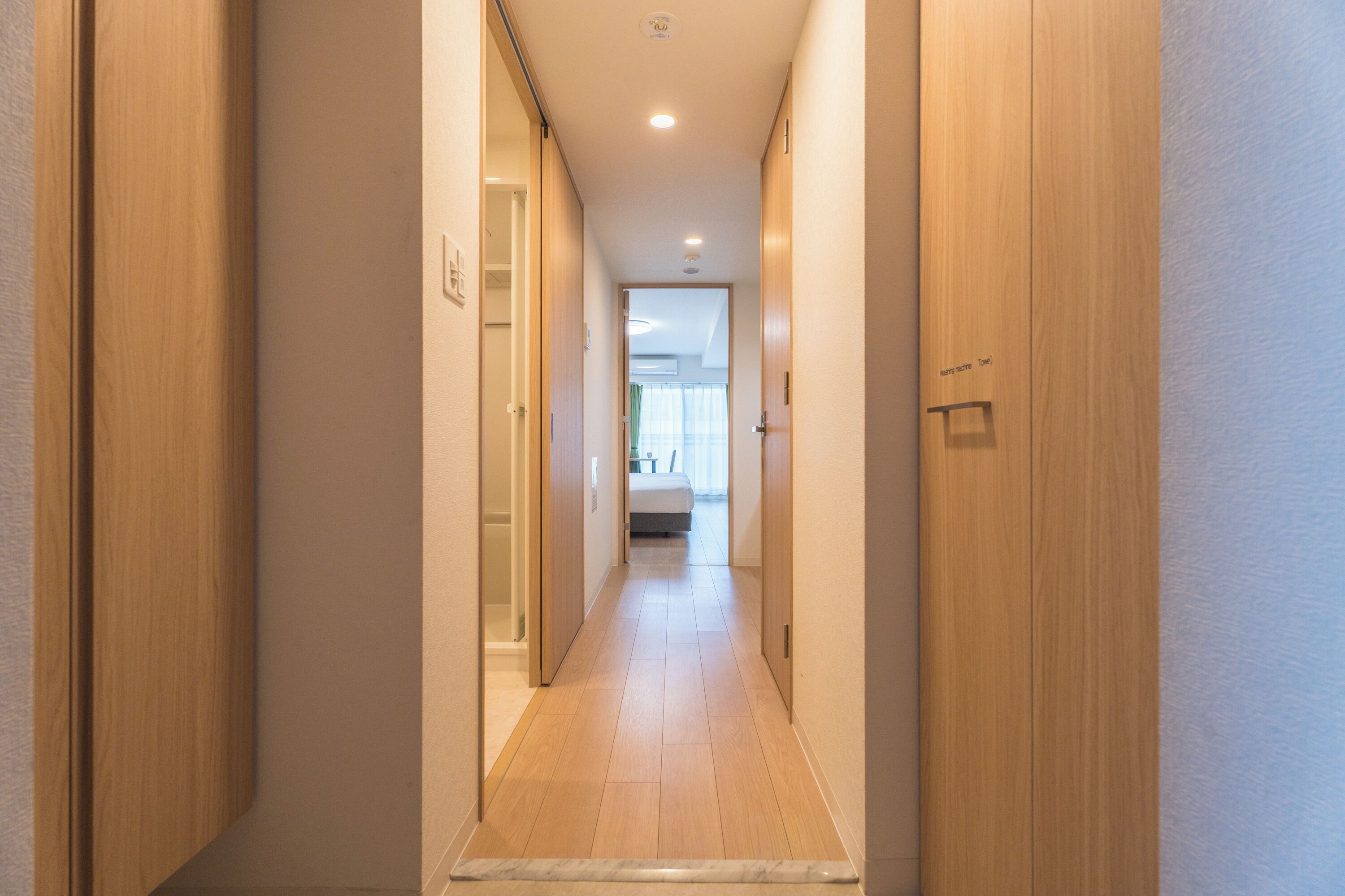 A hallway with wooden doors and a tiled floor leading to a room with a bed and a window.