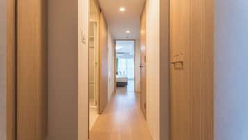 A hallway with wooden doors and a tiled floor leading to a room with a bed and a window.