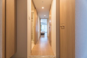 Een gang met houten deuren en een betegelde vloer die leidt naar een kamer met een bed en een raam.
