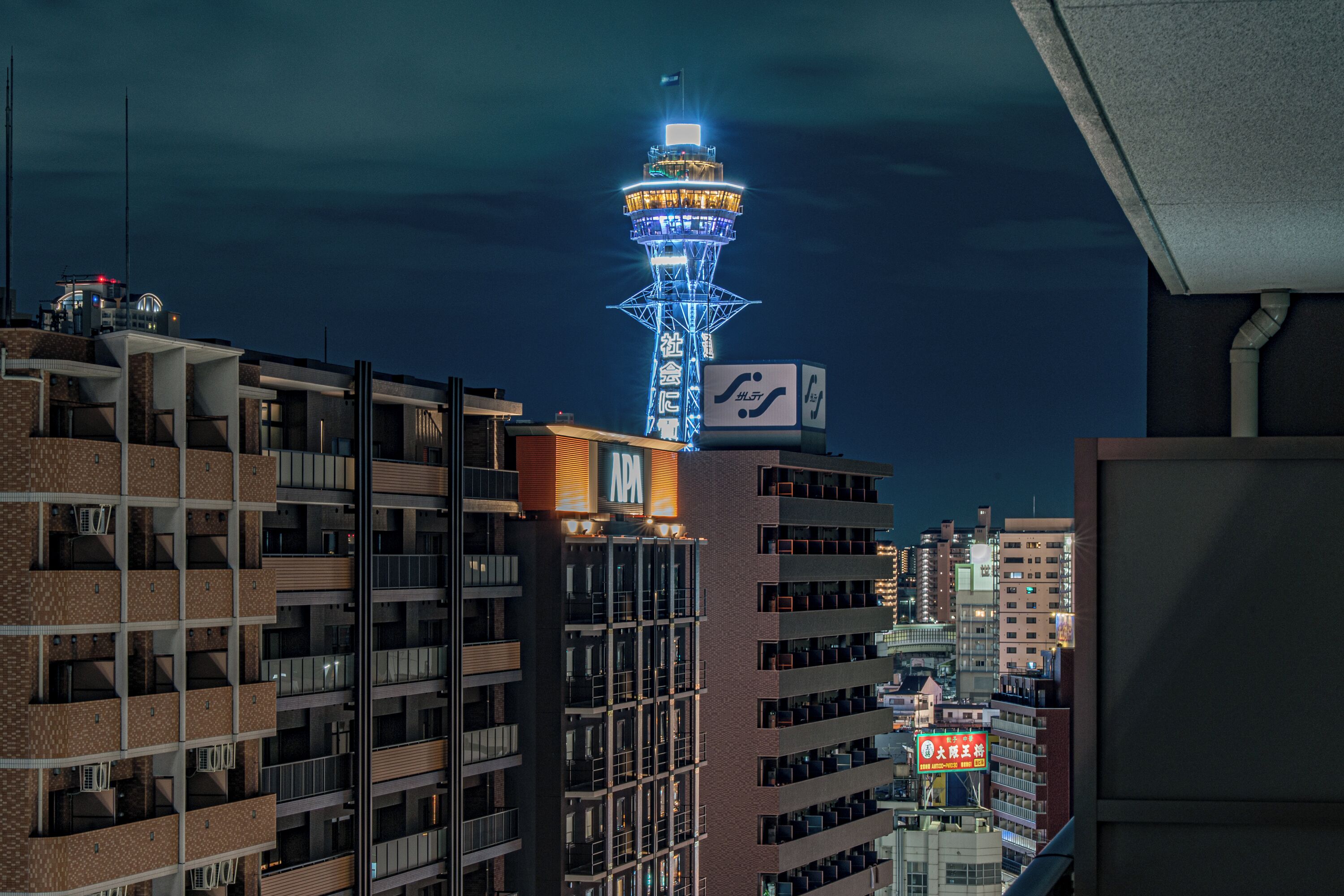 Een meerhoog gebouw met een opvallende toren en verlichte reclameborden.