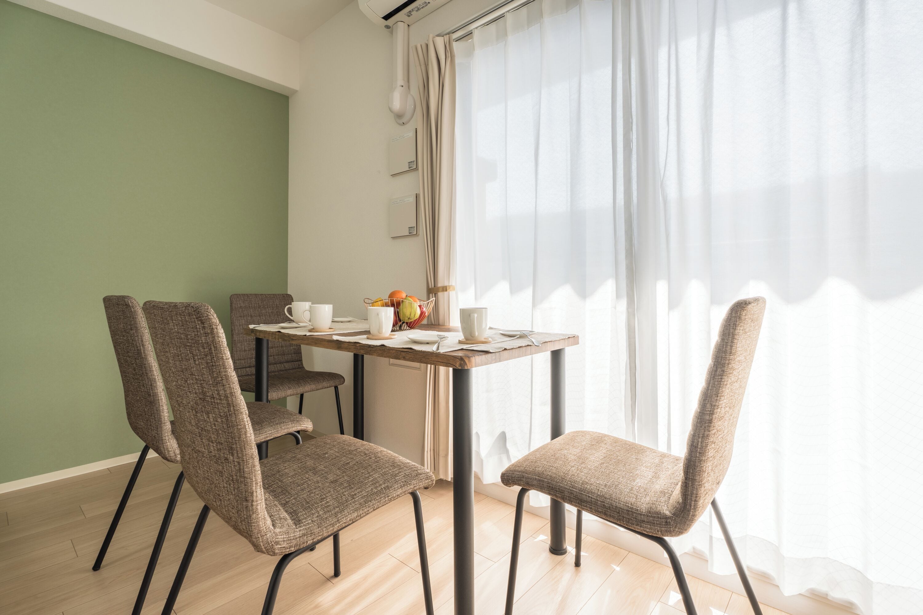 A dining area with a table set for four, chairs, and a window with sheer curtains.