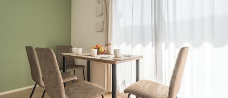 A dining area with a table set for four, chairs, and a window with sheer curtains.
