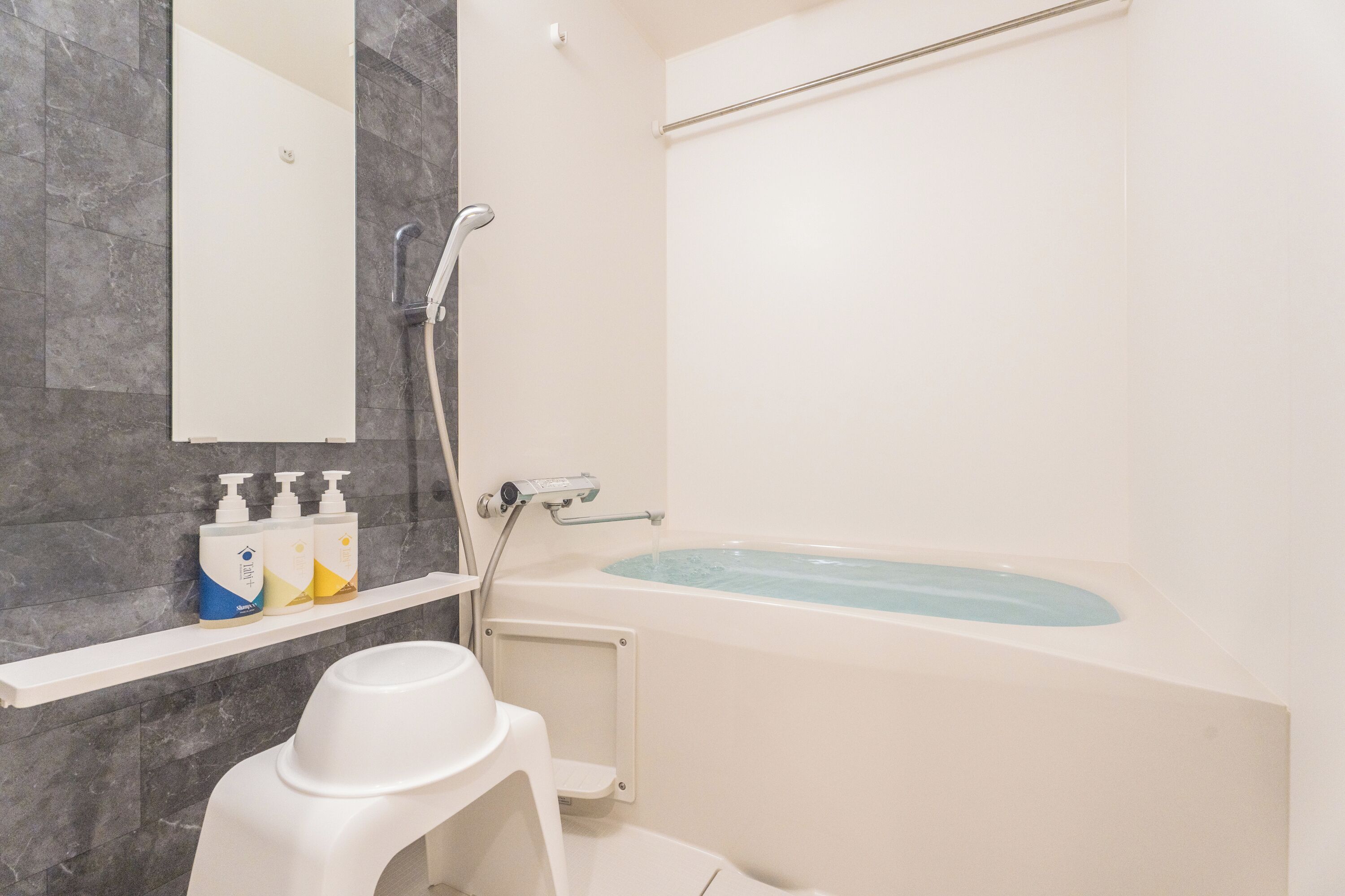 A bathroom with a bathtub, a shower, a toilet, and a shelf with toiletries.