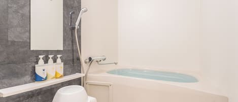 A bathroom with a bathtub, a shower, a toilet, and a shelf with toiletries.