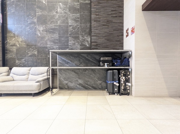 Un hall d’hôtel moderne avec un mur en marbre, un canapé, un porte-bagages et une petite table.