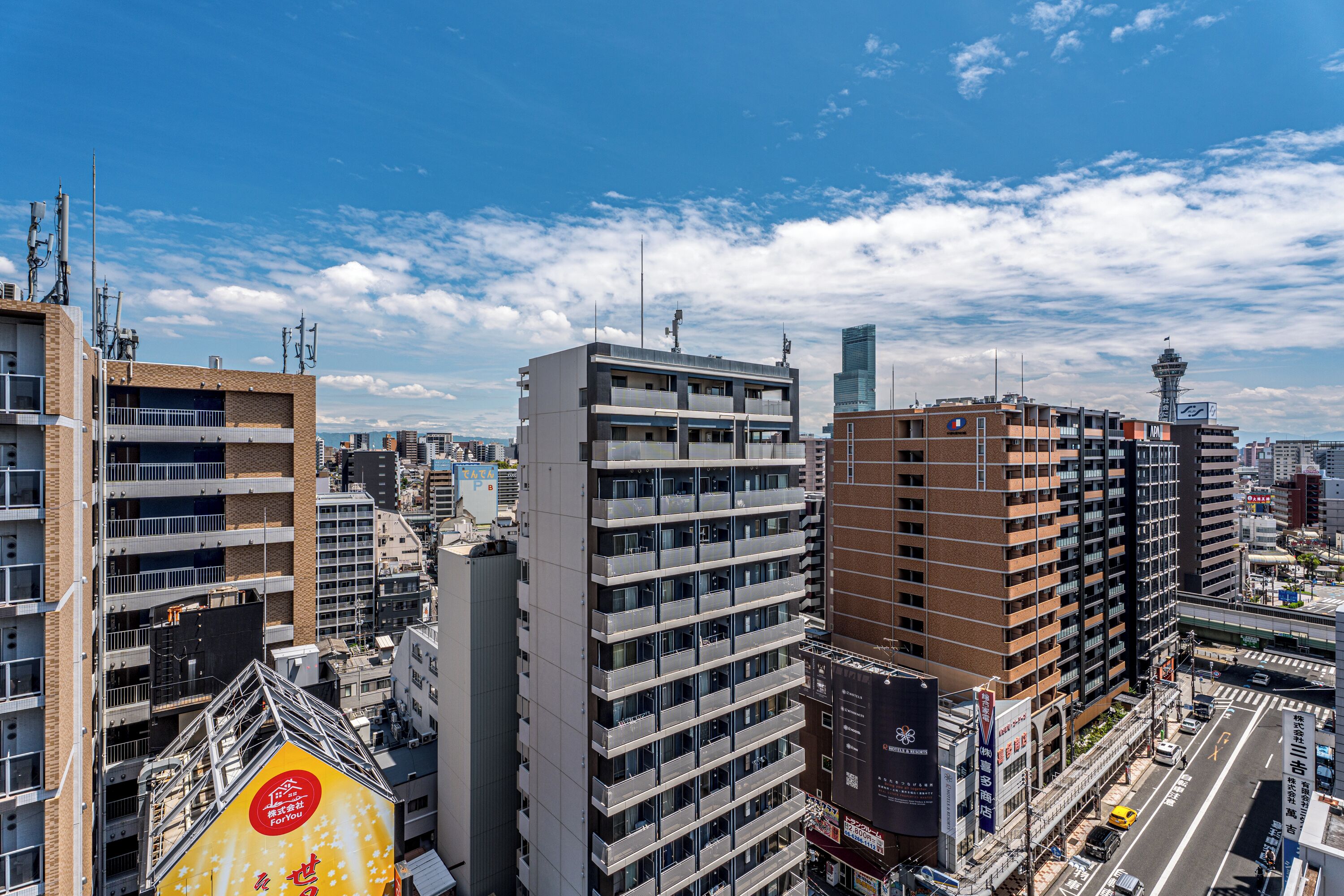 A high-rise building with multiple floors, a prominent sign with Japanese characters, and a clear blue sky with scattered clouds.